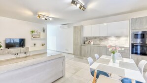 A modern living room with a flat-screen TV, a sofa, and a dining area with a table and chairs. - Central Msida | Modern, Bright & Comfortable (Msida)