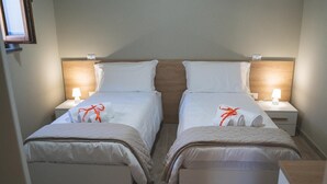 Habitación de hotel con dos camas individuales, cada una con una mesita de noche, una lámpara y ropa de cama bien ordenada con una toalla y un lazo.