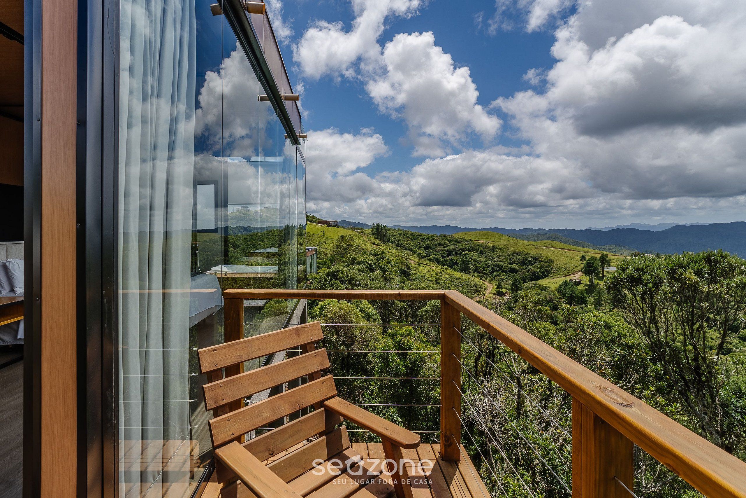 Un balcon doté d’une balustrade en bois, offrant une vue sur un paysage luxuriant avec des montagnes à l’horizon.