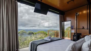Un dormitorio con un ventanal grande, una cama, un televisor de pantalla plana y techo de madera.