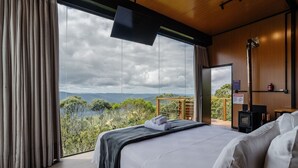 A bedroom with a large window, a bed, a flat-screen TV, and a wooden ceiling.