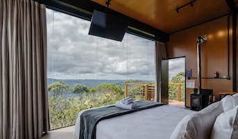 Quarto com uma janela grande, uma cama, uma TV de tela plana e teto de madeira.