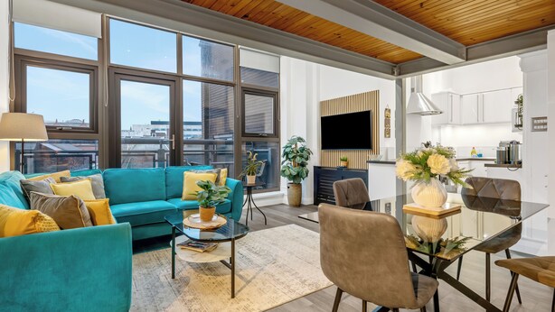 A modern living room with a teal sofa, a glass coffee table, and a dining area with a glass table and chairs. - Central Apt Old Market Sqr with Parking (Nottingham)