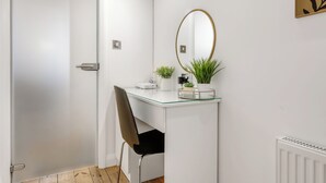A modern bathroom with a white vanity, a glass-top desk, a black chair, a round mirror, and a radiator. - Central Apt Old Market Sqr with Parking (Nottingham)