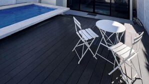 Una moderna casa a due piani con piscina, terrazza arredata e ampie finestre.