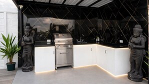 Una cucina esterna moderna con una griglia in acciaio inossidabile, mobili bianchi e due statue.