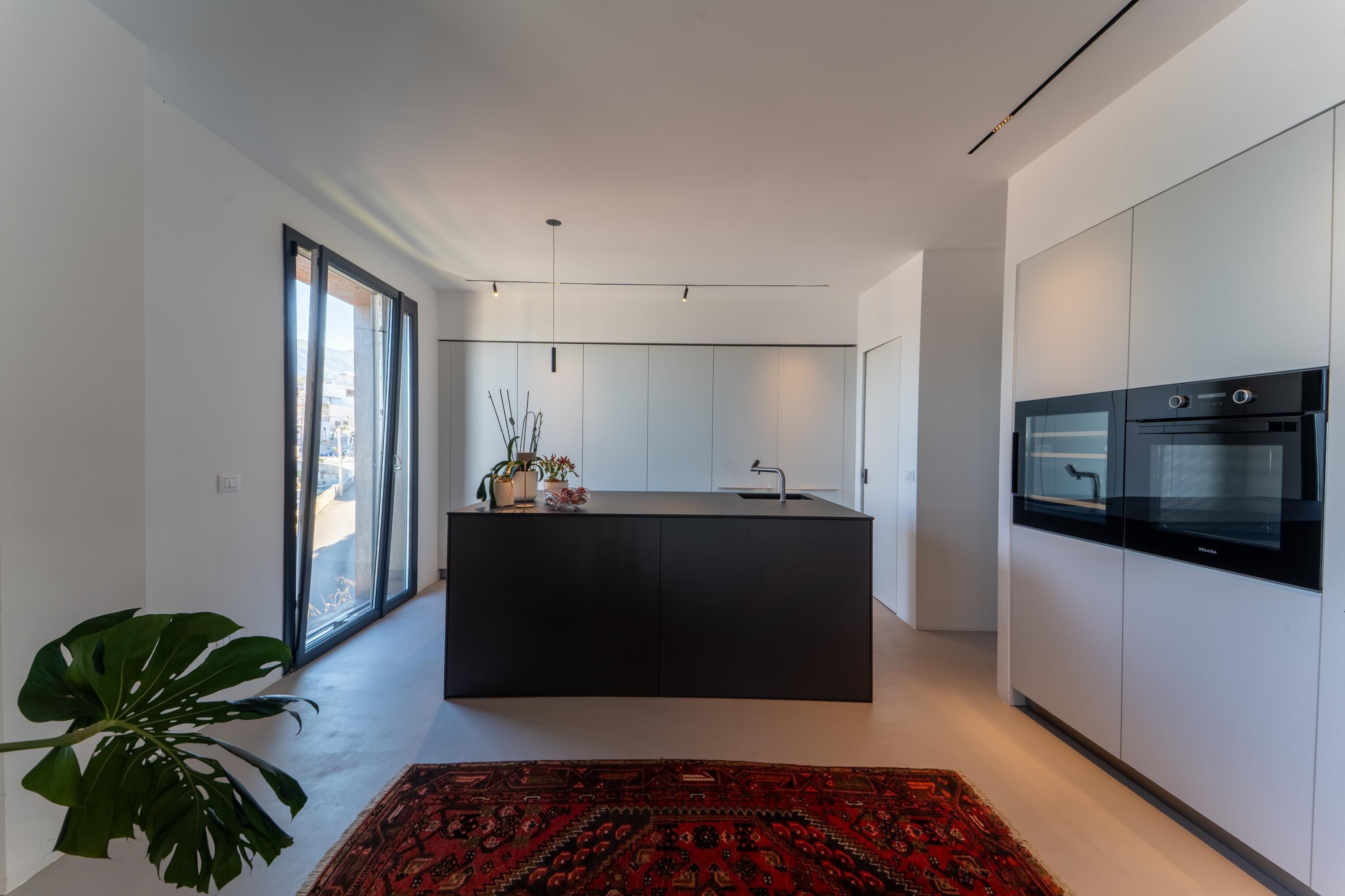 A modern kitchen with a central island, built-in appliances, and a large window.