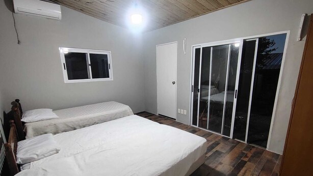 A bedroom with two beds, a window, a sliding glass door, and an air conditioning unit.