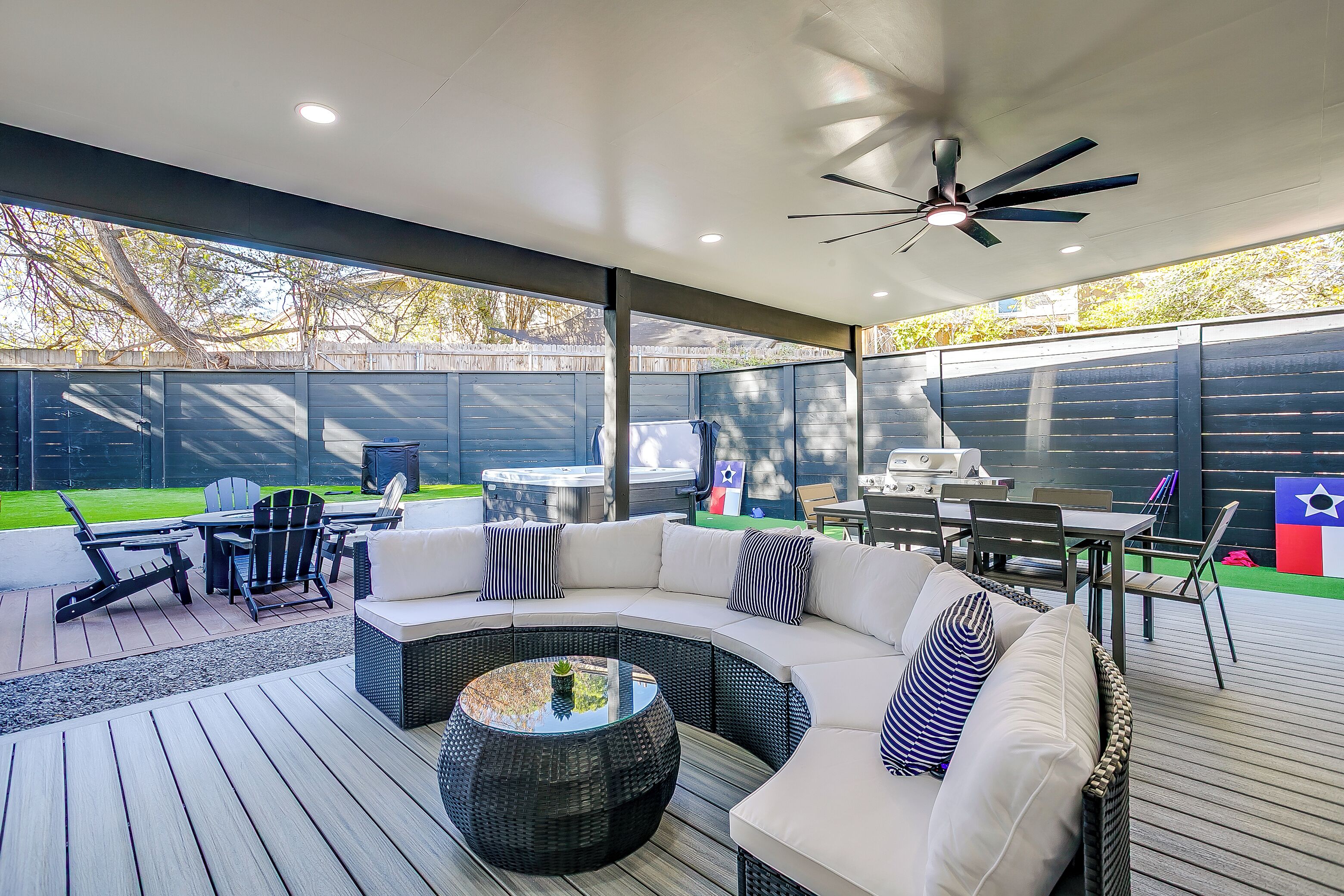 A covered outdoor patio with a curved white sofa, black wicker coffee table, and dining area with chairs and a table.