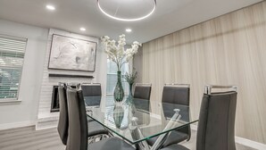 Una sala de reuniones moderna con una mesa de vidrio, sillas de cuero, un jarrón con flores blancas, una chimenea y un cuadro abstracto grande en la pared.