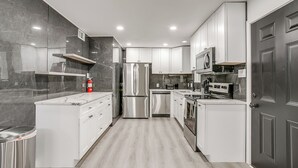 Una cocina moderna con armarios blancos, electrodomésticos de acero inoxidable y una salpicadera de mármol.