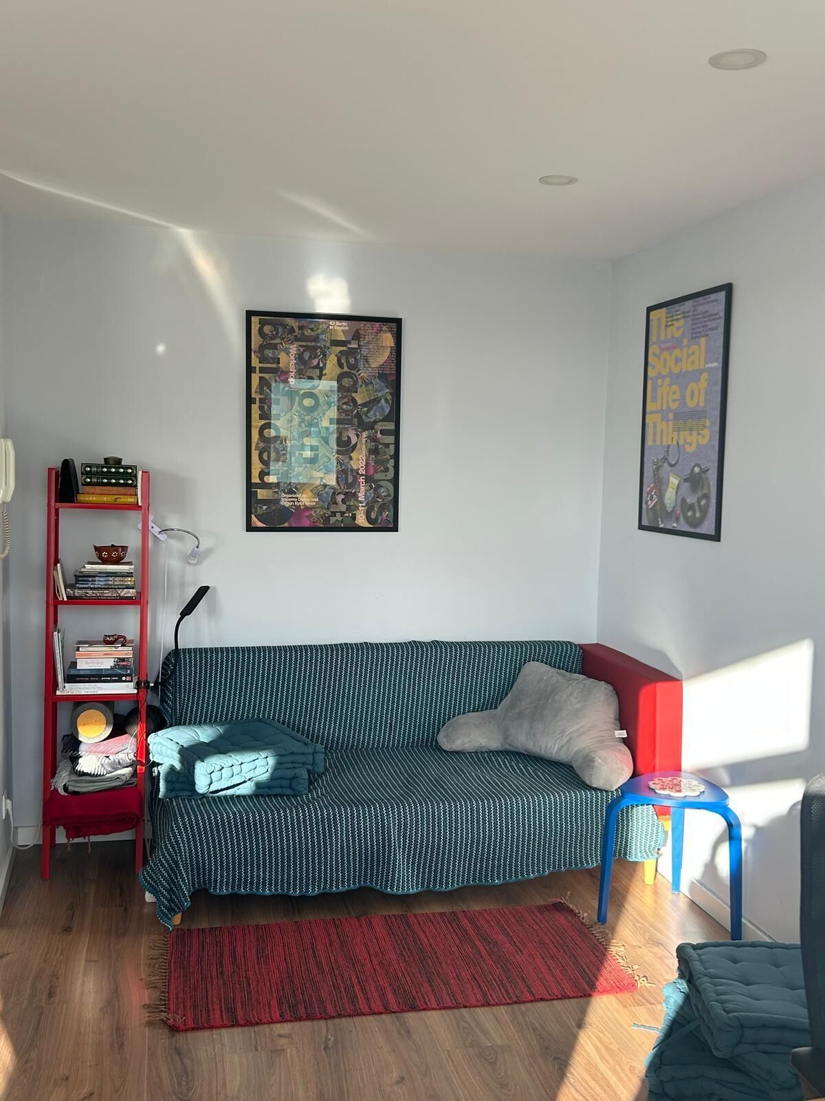 Un salón acogedor con un sofá estampado, una estantería roja y un póster enmarcado en la pared.