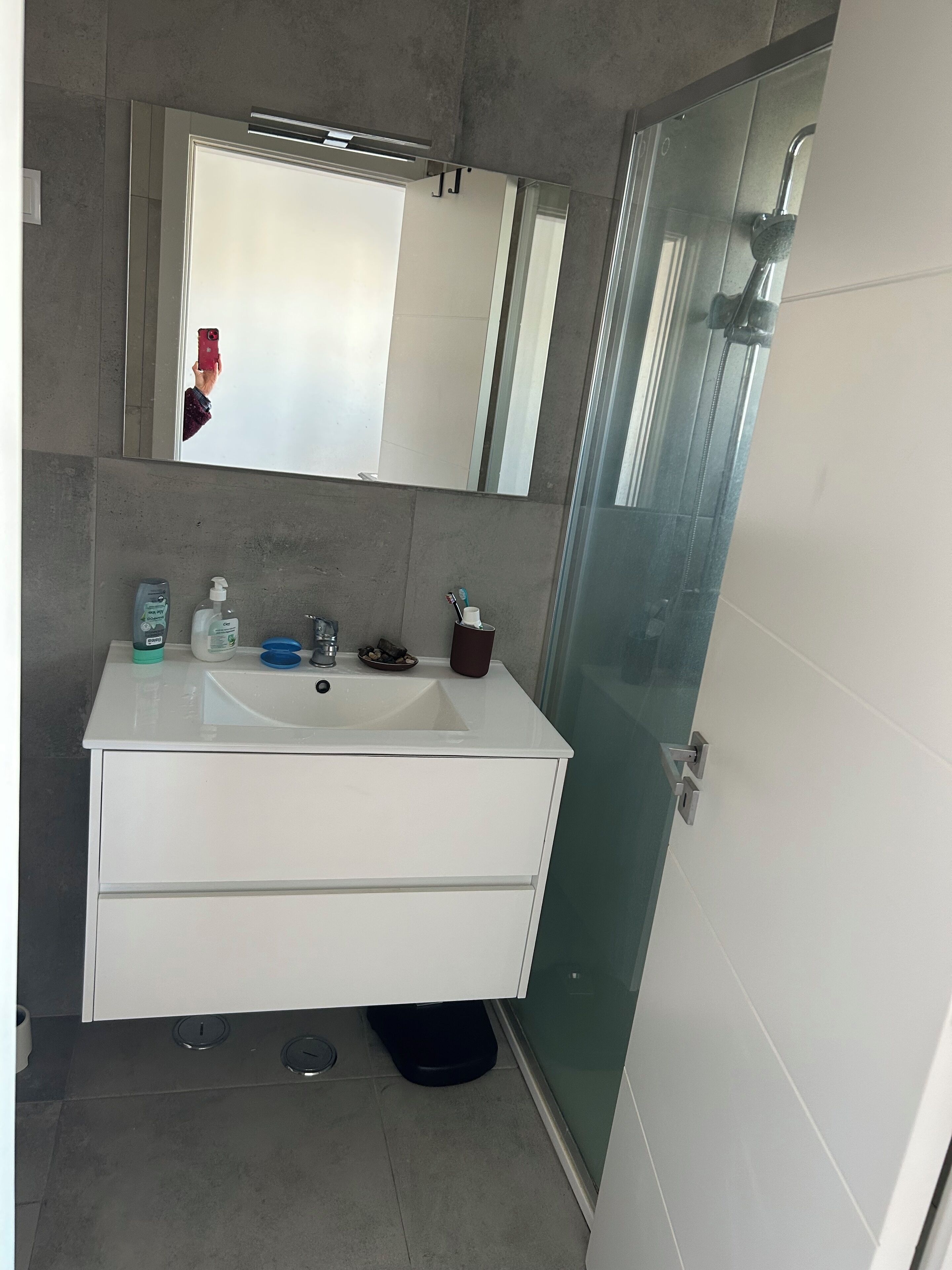 Ein modernes Badezimmer mit einem weißen Waschtisch, einem großen Spiegel und einer Duschkabine aus Glas.