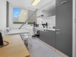 A modern kitchen with white chairs, a wooden table, a microwave, and grey cabinets.