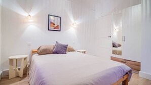 A modern bedroom with a large bed, bedside tables, a mirror, and wall-mounted lights. - Le spot idéal à Lorient neuf, spacieux & chic (Lorient)