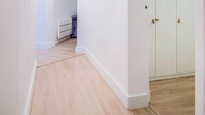 A narrow hallway with wooden flooring and white walls, leading to a room with a bed and a wardrobe. - Le spot idéal à Lorient neuf, spacieux & chic (Lorient)