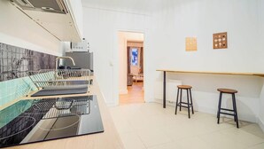 A modern kitchen with a built-in oven, a dishwasher, and a countertop with a sink. There are two stools and a wooden bar counter. - Le spot idéal à Lorient neuf, spacieux & chic (Lorient)