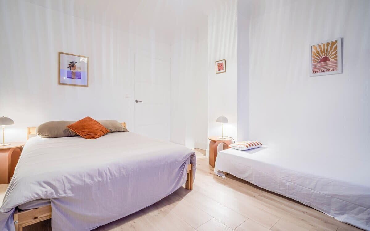 Une chambre avec deux lits, une table de chevet et une lampe fixée au mur.