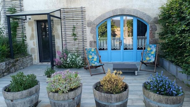 Un cortile con una porta blu, un'area salotto coperta e quattro fioriere in legno con diverse piante.