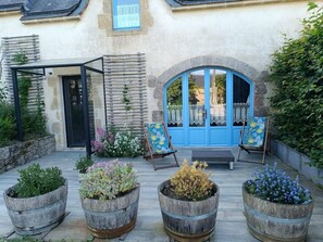 A courtyard with a blue door, a covered seating area, and four wooden planters with various plants. - Longère de caractère, calme et grand confort (Pluneret)