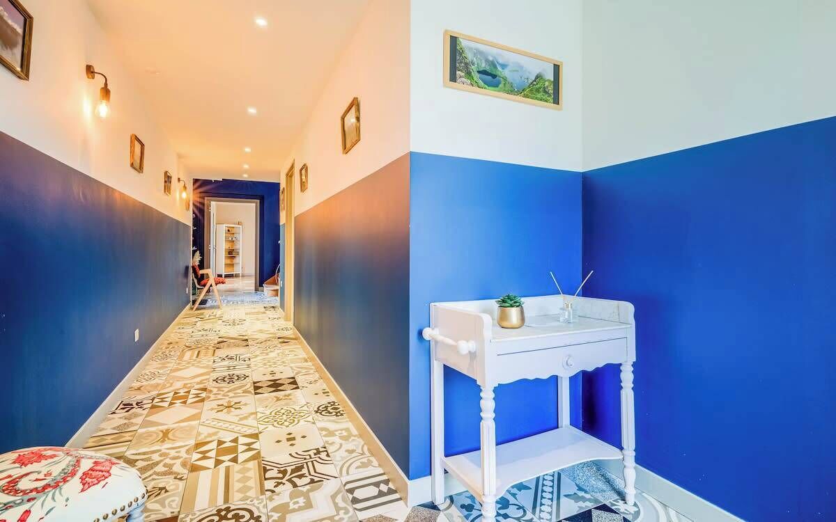 Un couloir doté d’un sol à motifs, une console blanche ornée d’une plante et un tableau encadré accroché au mur.
