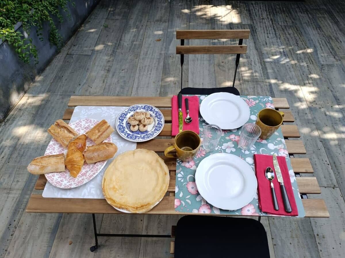 Une table en bois dressée à l’extérieur, avec des assiettes, des couverts et de la nourriture.