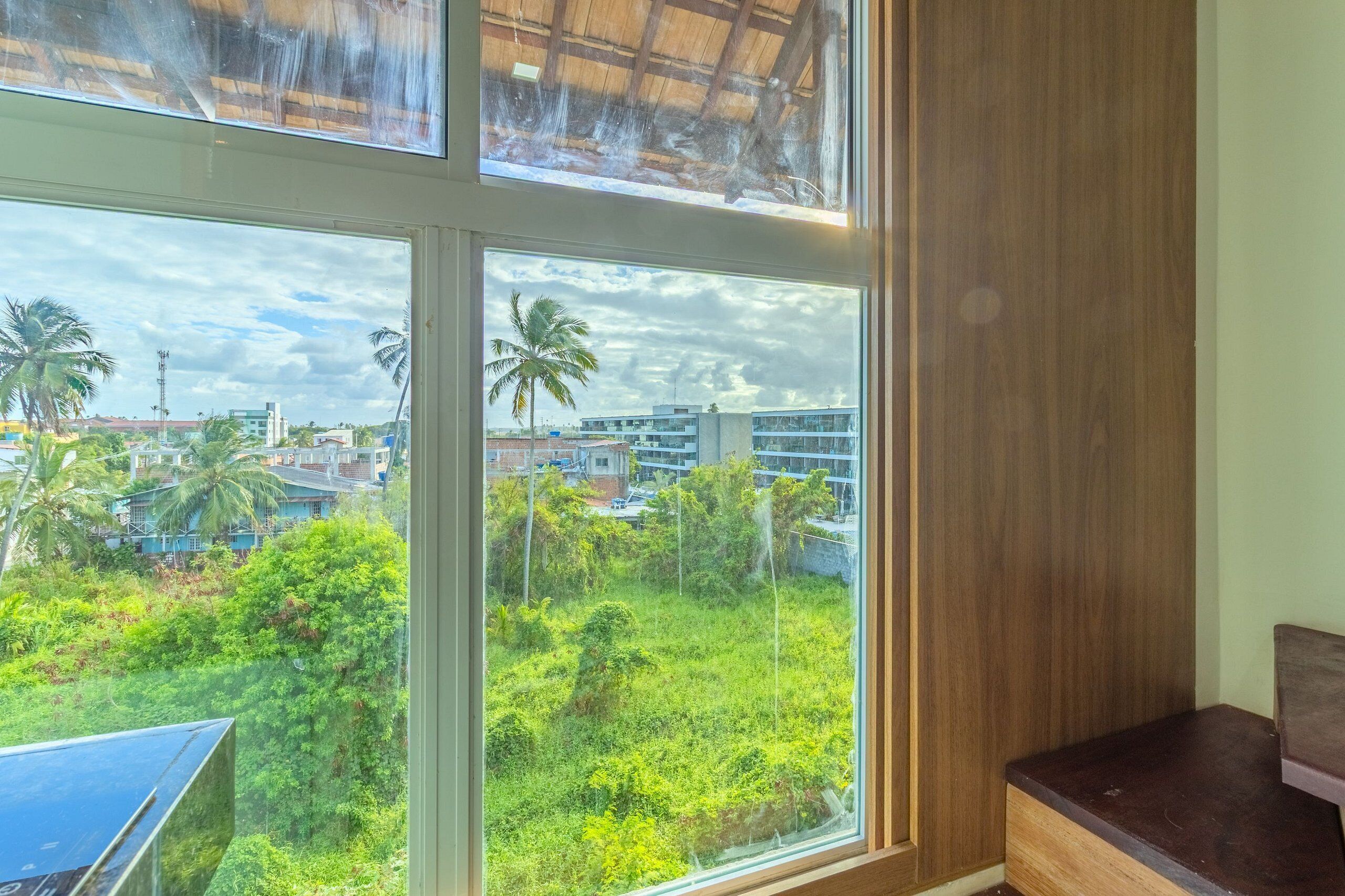 A room with a large window offering a view of a green area with trees and buildings.