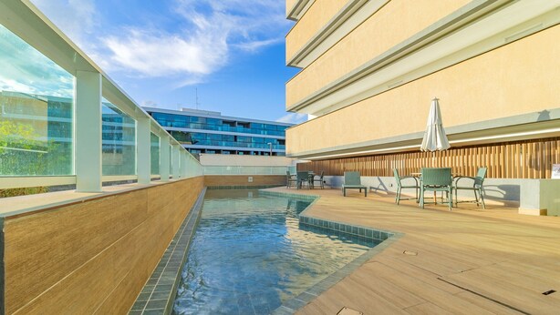 Zona de piscina en la azotea con terraza de madera, mobiliario exterior y vista a un edificio moderno al fondo.