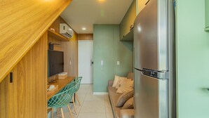 Cocina compacta con encimera de madera, refrigerador empotrado y comedor con una silla y mesa.