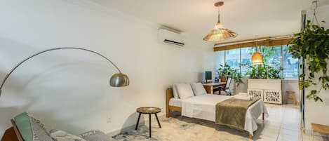 A modern bedroom with a bed, bedside table, and a desk. There is a window with a view of the outside.