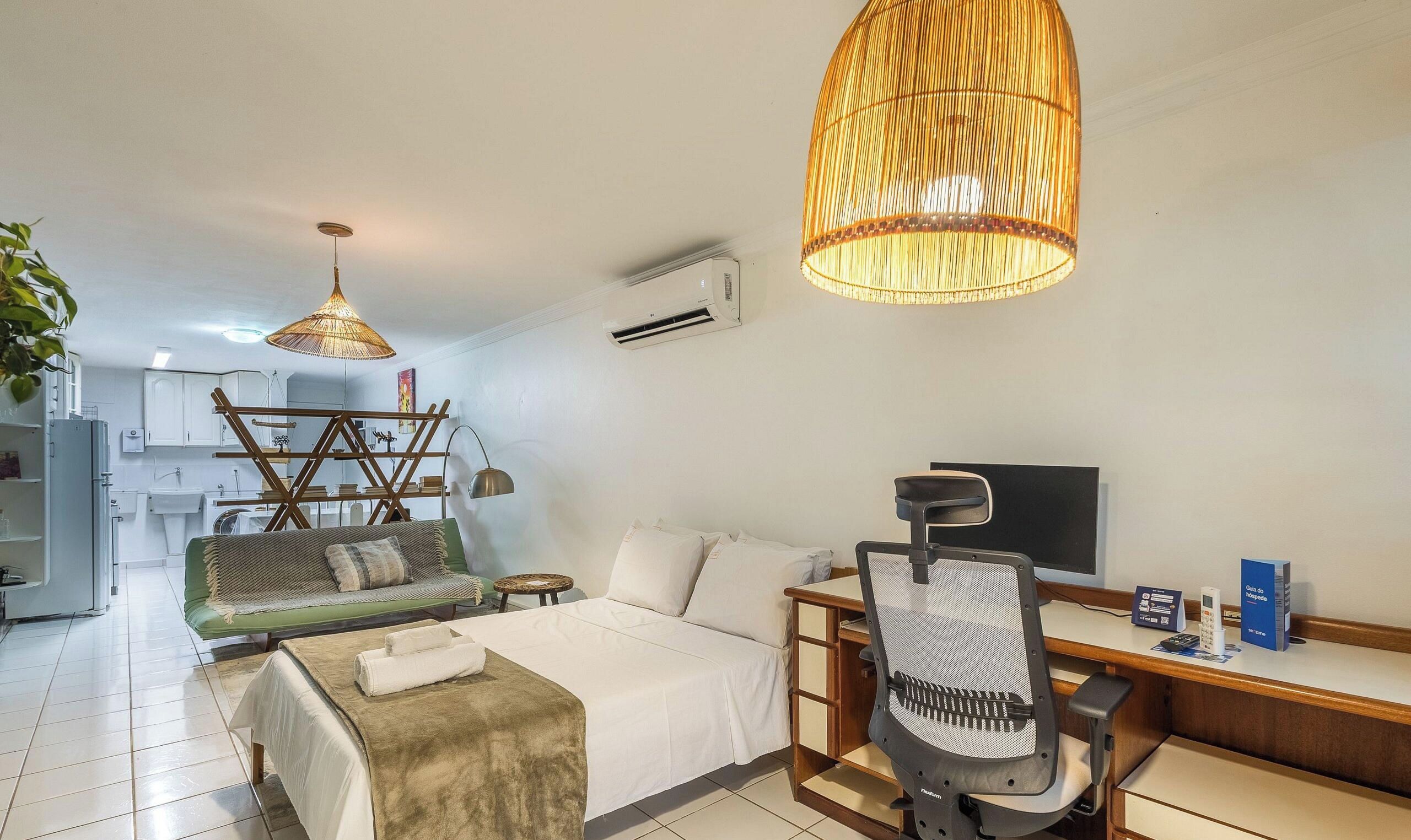 Una habitación de hotel moderna con una cama, un escritorio con una computadora, una silla y una lámpara colgante grande.