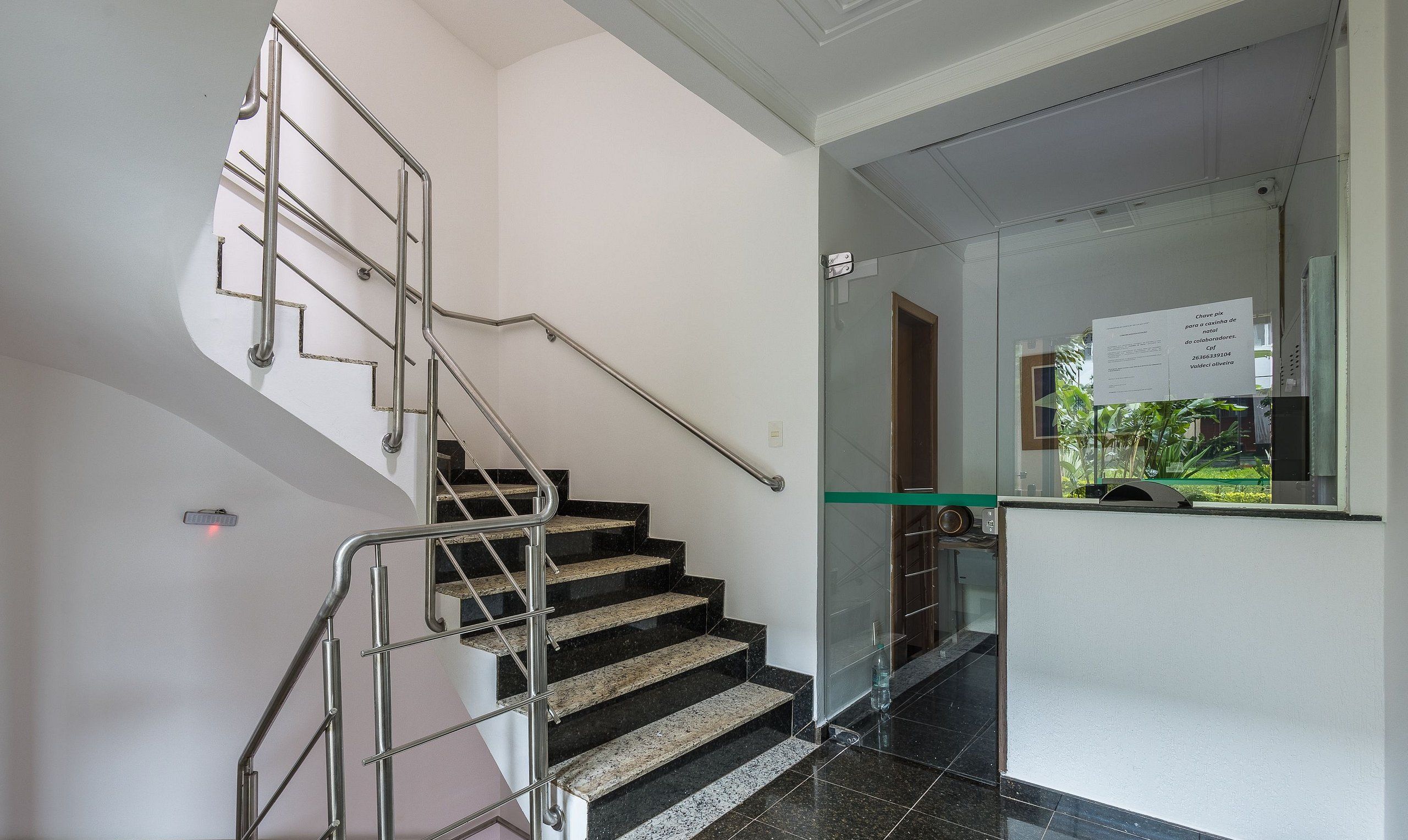 A staircase with metal handrails, black and beige steps, and a glass door leading to a reception area with a sign.