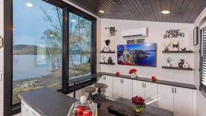 A modern kitchen with a large window overlooking a lake, a mounted TV, and decorative shelves.