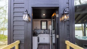 A modern kitchen with white cabinets, a black countertop, and a refrigerator. There are two wall-mounted lanterns on either side of the entrance.