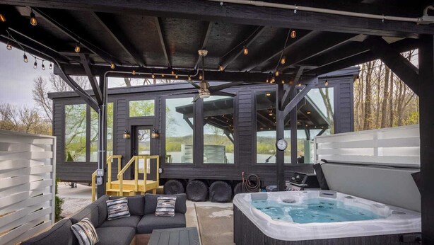 A covered outdoor area with a hot tub, a sofa set, and a wooden deck.