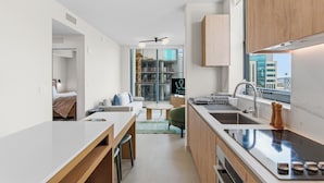 Una cocina moderna con estufa integrada, un lavamanos y armarios de madera. Hay una zona de comedor con una mesa y sillas, y vistas a la ciudad a través de amplios ventanales.