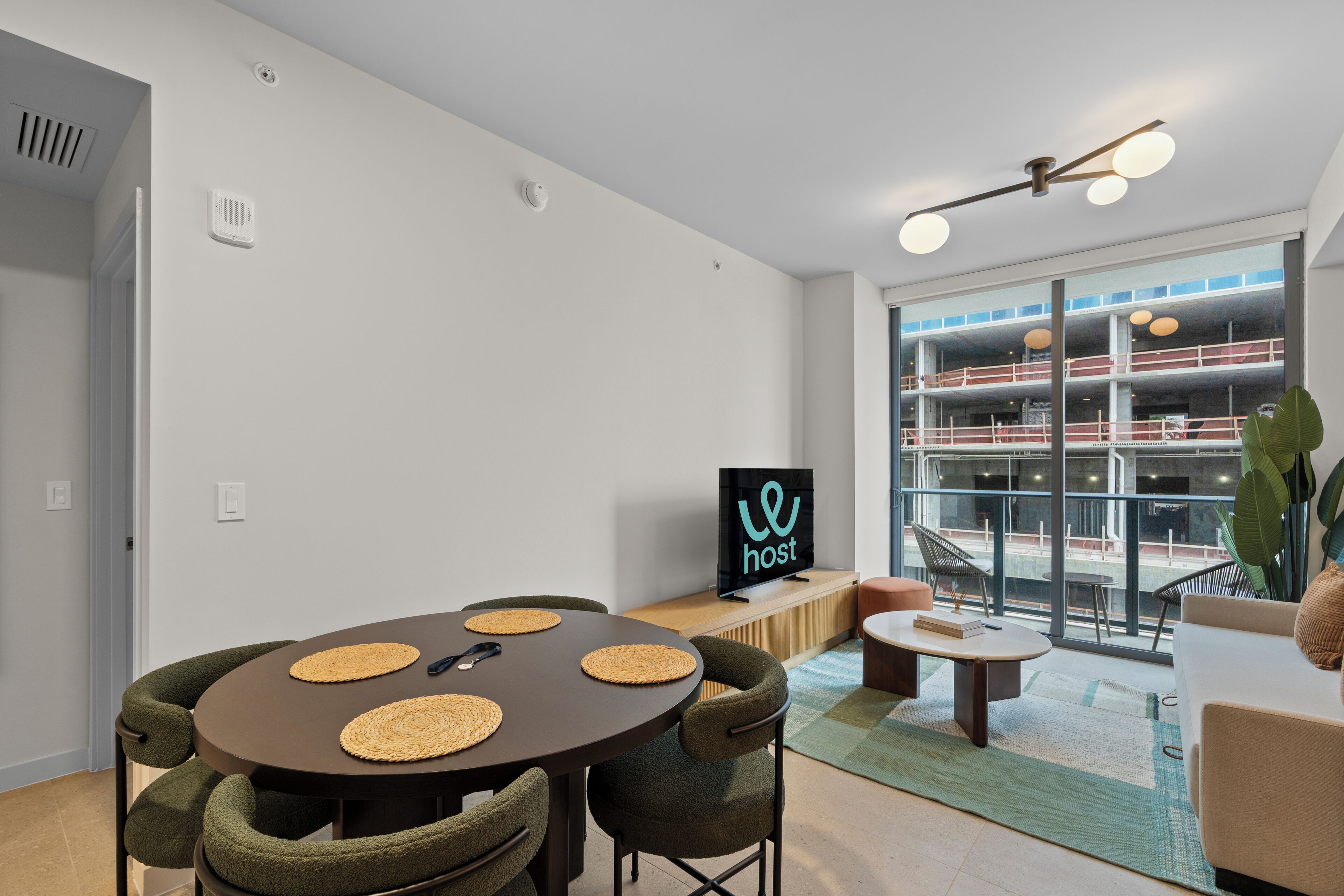 Un salon moderne comprenant un coin repas, un téléviseur et un balcon offrant une vue sur un immeuble.