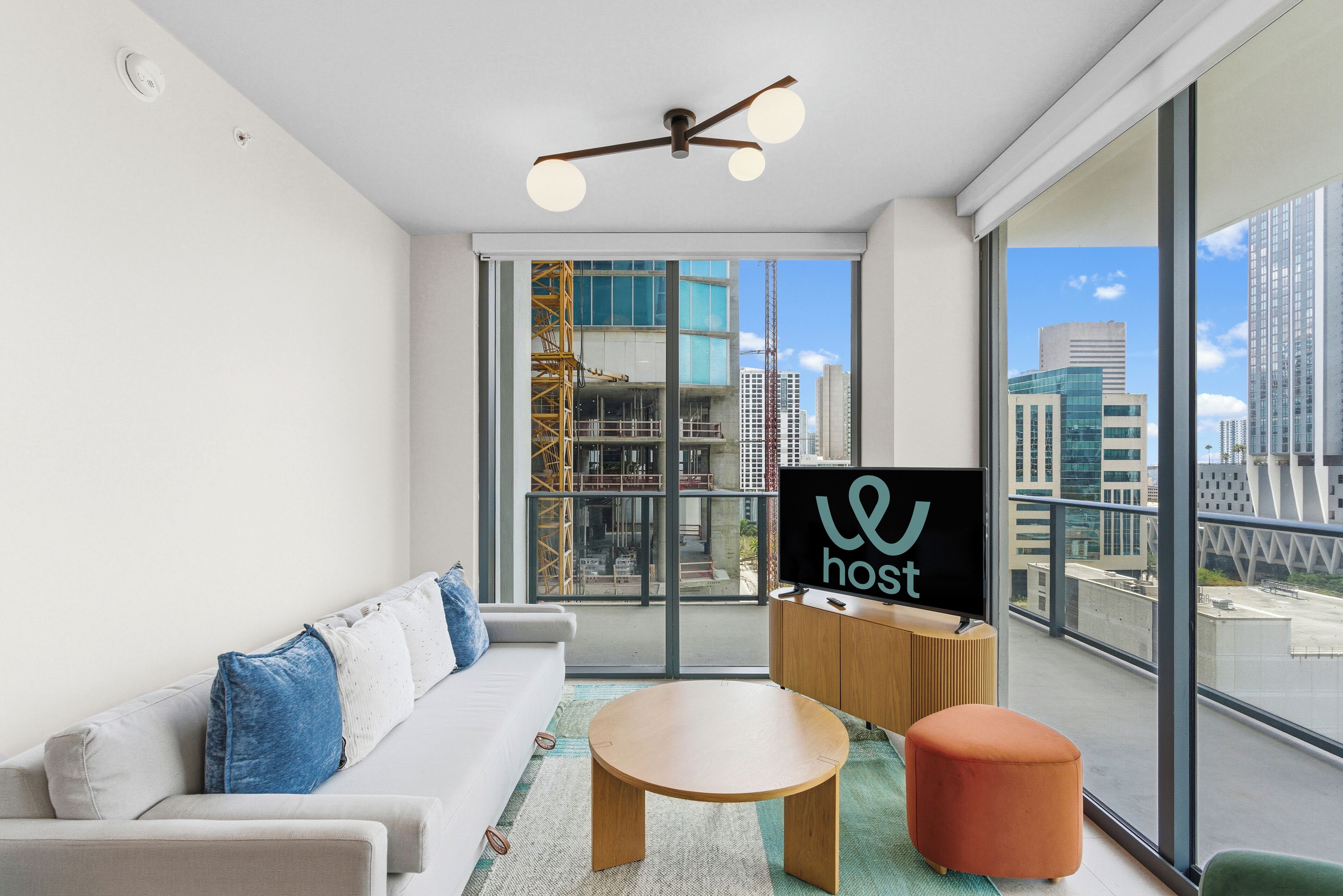 A modern hotel room with a large window, a sofa, a round wooden table, and a television.
