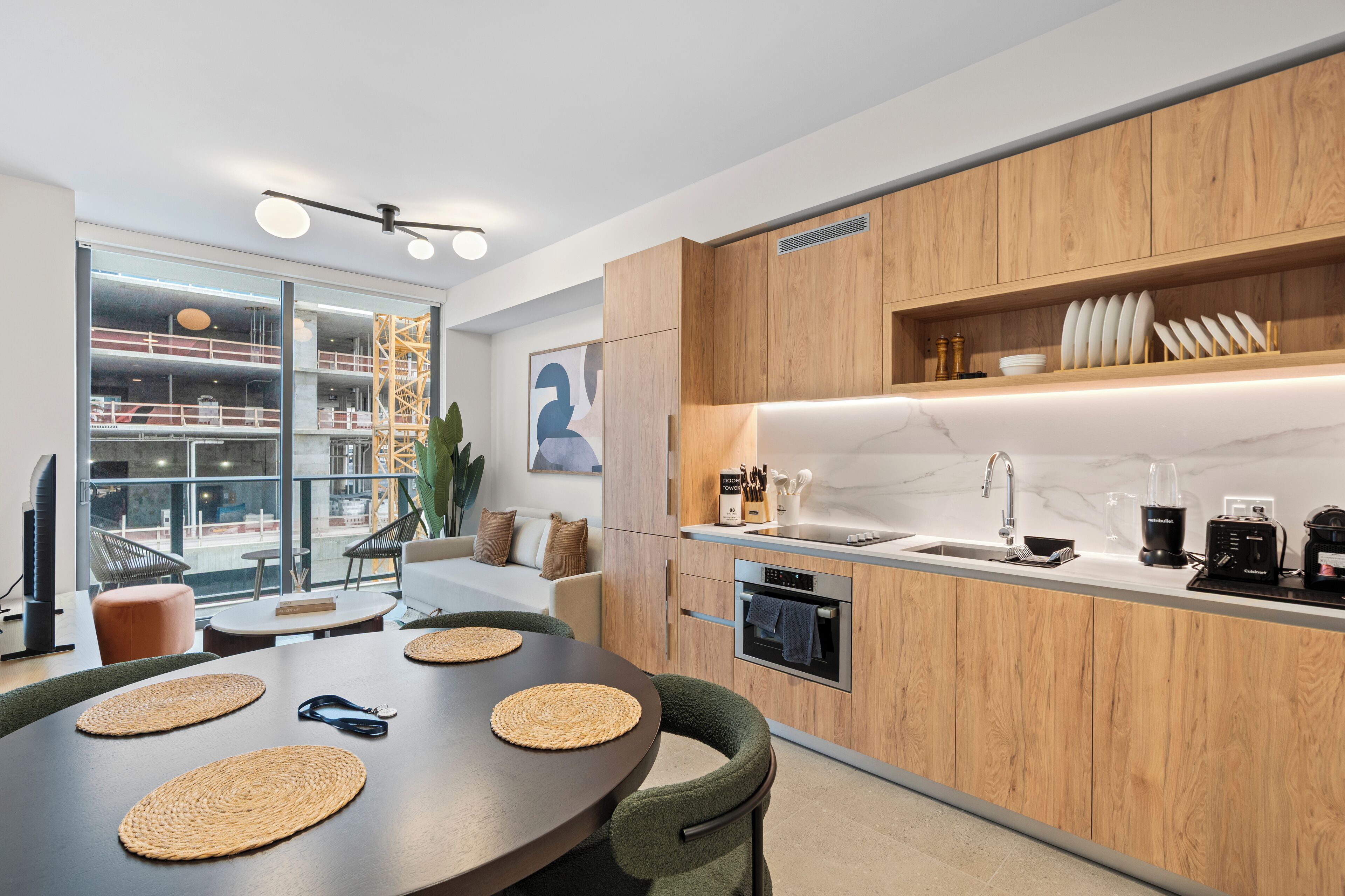 Une cuisine moderne avec des meubles en bois, un four encastré et une grande fenêtre donnant sur un chantier de construction.