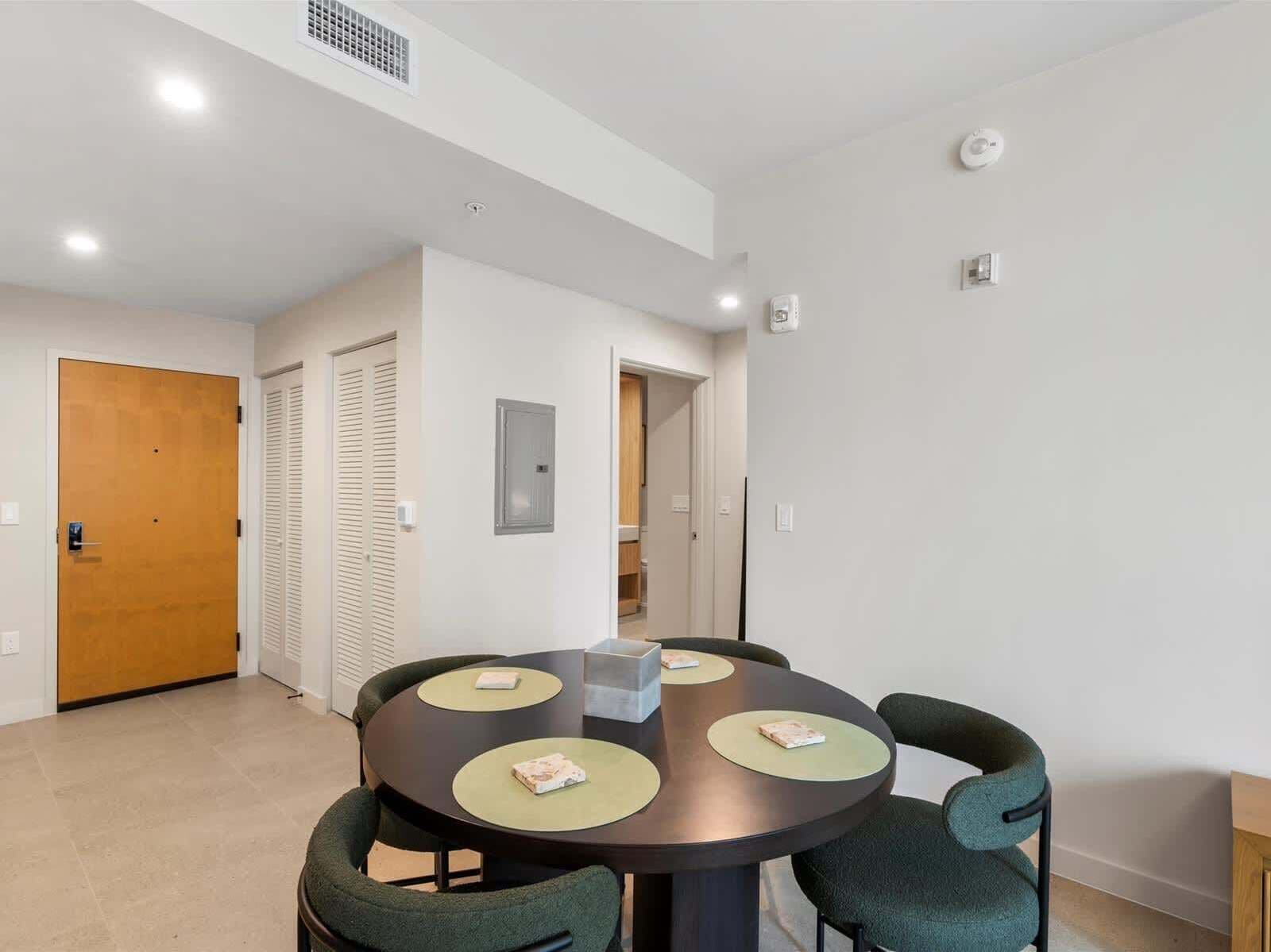 A modern room with a round table, four chairs, a wooden door, and a white wall.