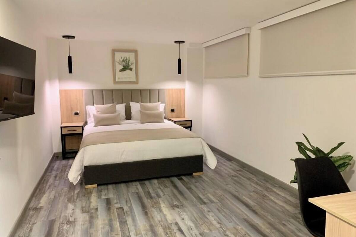 Ein modernes Schlafzimmer mit einem großen Bett, zwei Nachttischen, einem Schreibtisch und einem Sessel.