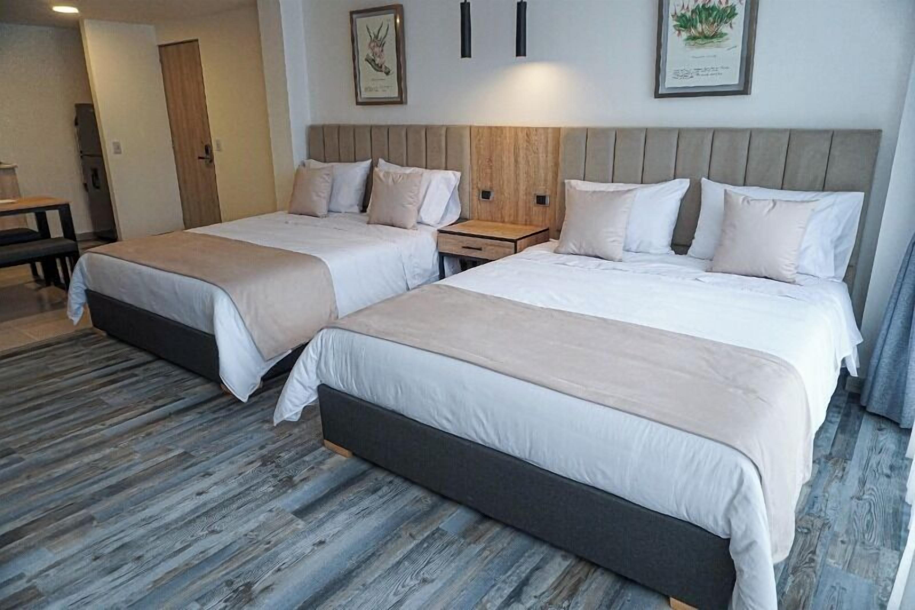 A hotel room with two beds, wooden headboards, a small bedside table, and a bench.