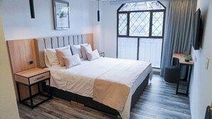 A modern bedroom with a large bed, wooden headboard, bedside tables, a window with curtains, and a mounted TV. - Hotel 86 Suites (Bogotá)