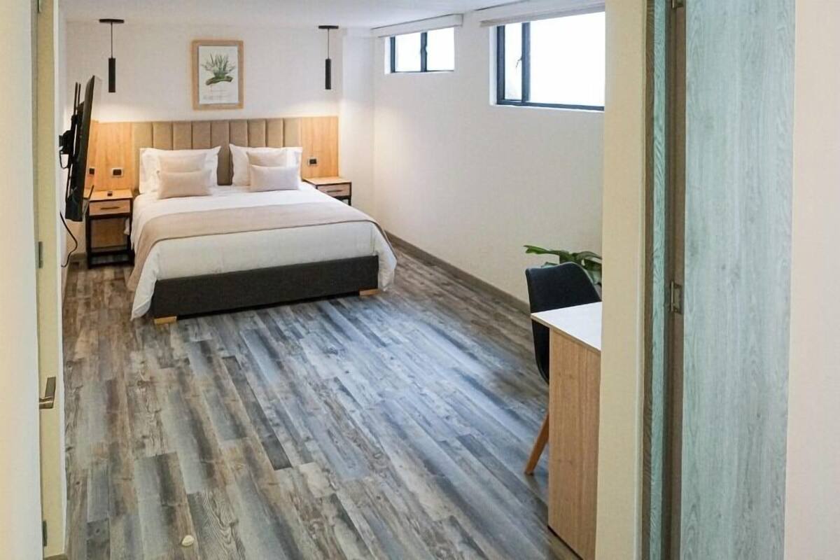 Ein modernes Schlafzimmer mit einem großen Bett, Holzboden, einem Schreibtisch und einem Fenster.