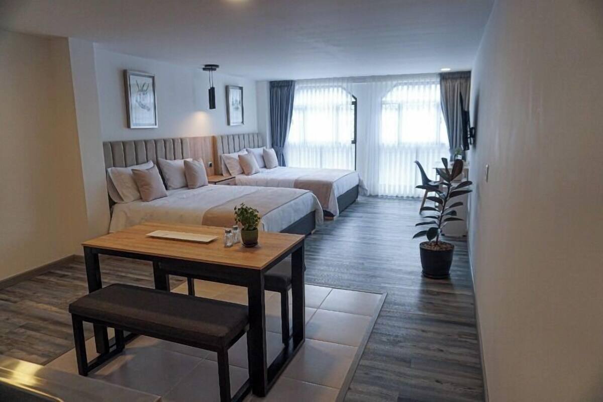 Ein modernes Hotelzimmer mit zwei Betten, einem Holztisch, einer Bank und einem Blumentopf.