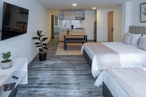 A modern hotel room with a large bed, a small desk, a potted plant, and a view of the kitchen and living area. - Hotel 86 Suites (Bogotá)