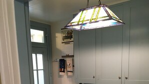 Una cocina con gabinetes azul claro, encimera blanca, lámpara colgante de vitral y una ventana con persianas.