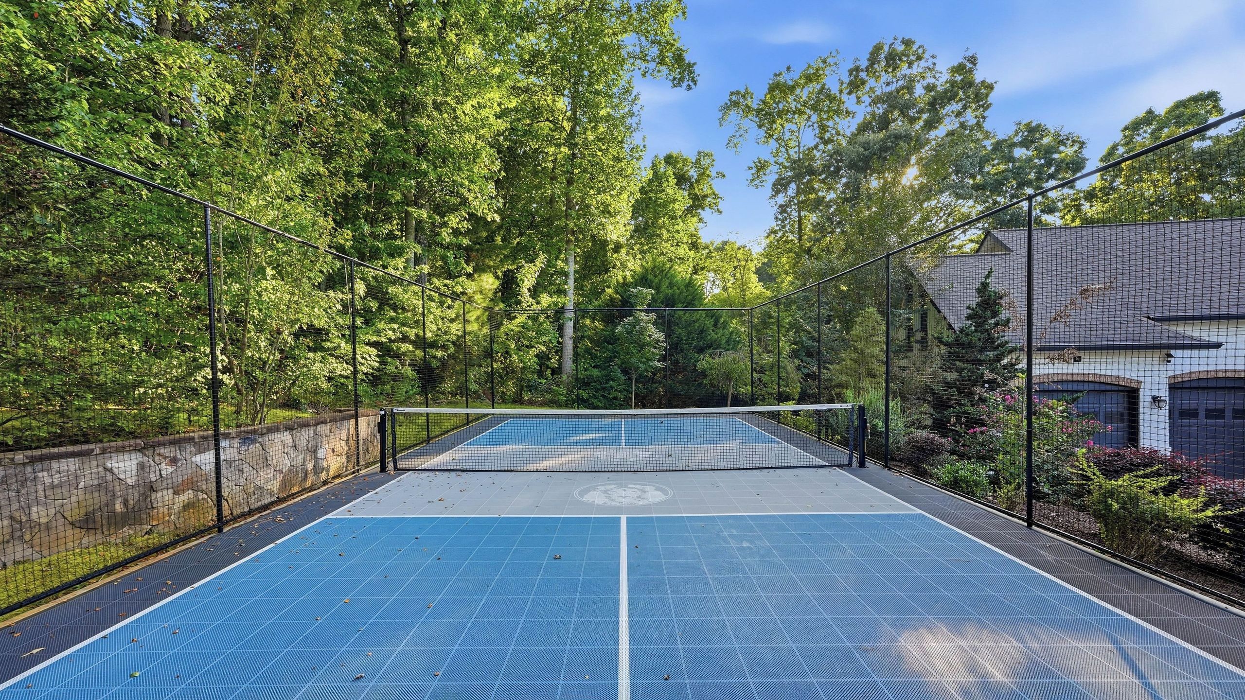 Un campo da tennis all'aperto circondato da una recinzione, con alberi e un edificio sullo sfondo.