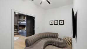 A modern living room with a curved sofa, a flat-screen TV mounted on the wall, and a staircase leading to a loft bedroom. - Lion Manor by Avantstay Spacious Lake Norman Home Hot Tub + Tennis Court + Firepit + Deck (Denver)