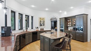 A modern kitchen with a central island, dark cabinetry, and a large window providing natural light. - Lion Manor by Avantstay Spacious Lake Norman Home Hot Tub + Tennis Court + Firepit + Deck (Denver)